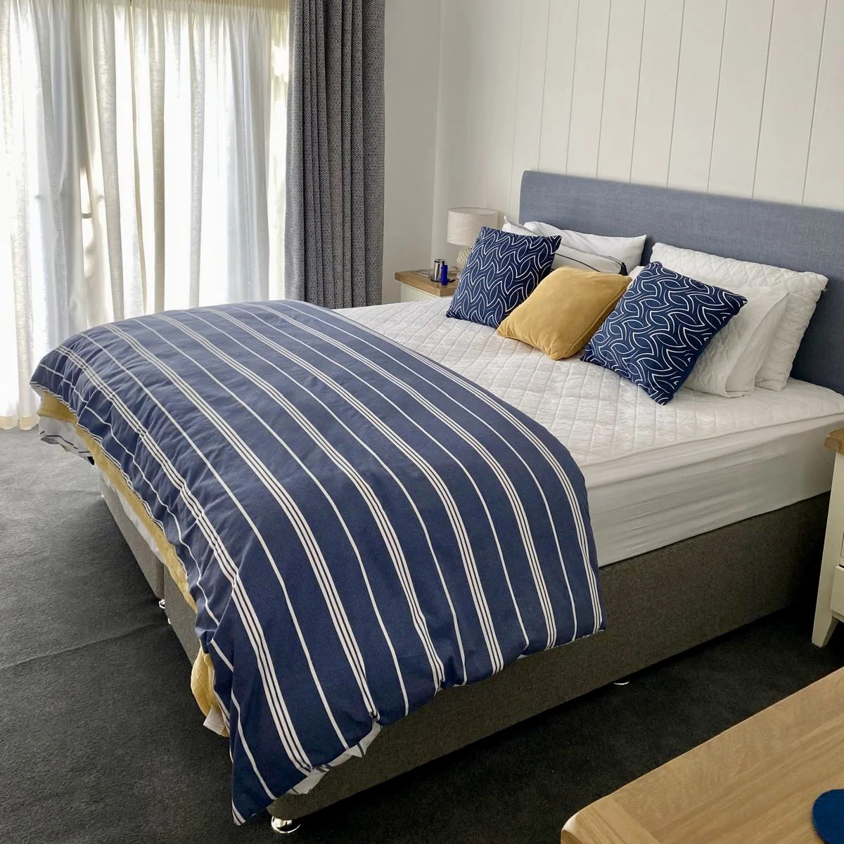 Master double bed with folded, striped cover and grey and yellow pillows